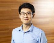 Professor Jerry Li stands against a wood paneled background